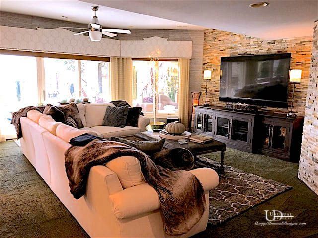 Living room with white sectional sofa, large TV on stone wall, green carpet.