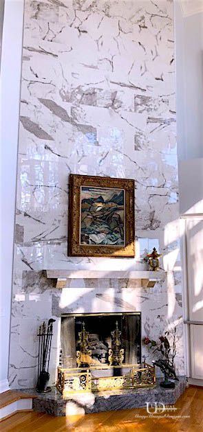 Marble fireplace with artwork, wooden floor, and sunlight.