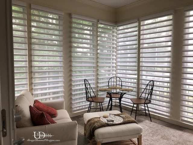 Sunroom with sheer window coverings, small table, chairs, sofa, and ottoman.