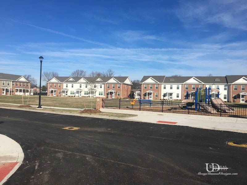 Row houses with a playground and street in front, under a blue sky.