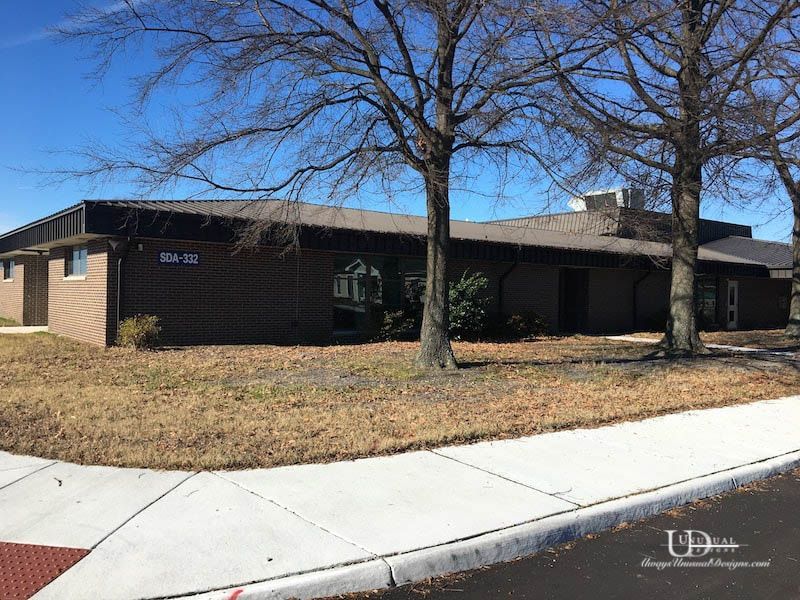Brick building with brown roof, trees, and blue sky.