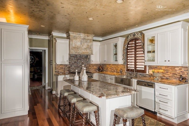 Elegant kitchen with white cabinets, island with stools, granite countertops, and decorative backsplash.