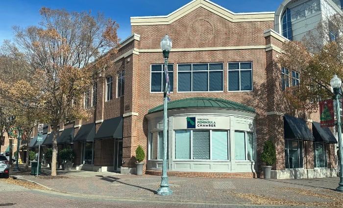 Brick building with black awnings and a green-roofed entrance; street with leafless trees.