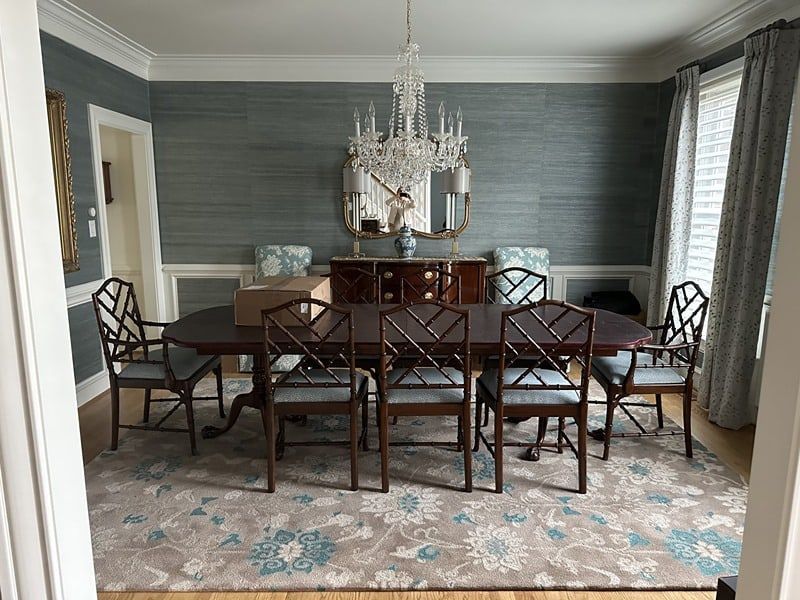 Formal dining room with dark wood table and chairs, blue textured wallpaper, chandelier, and patterned rug.