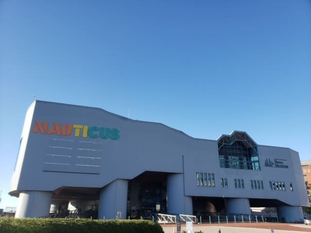 Nauticus Museum building with a gray exterior and colorful logo, under a clear blue sky.