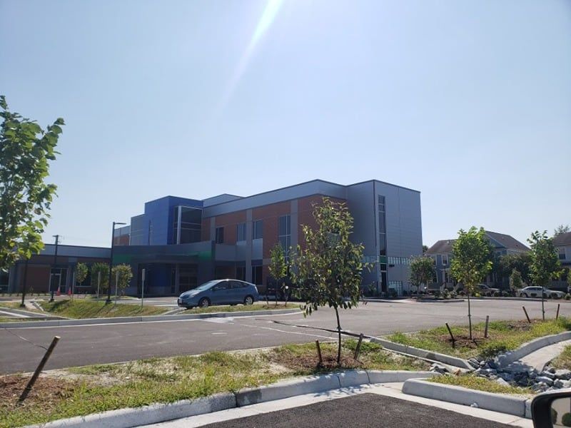 Modern building with gray, blue, and brick facade under a bright sky, car parked in front.