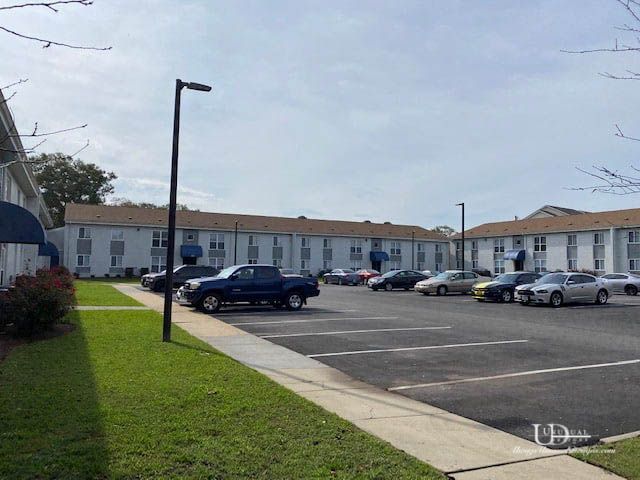 Parking lot with cars in front of two-story apartment buildings under a blue sky.
