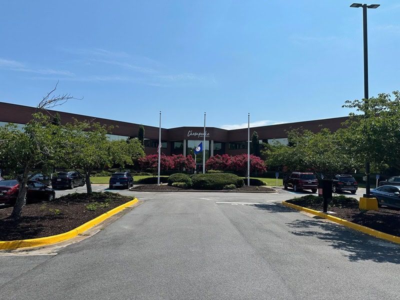 Draper building with a sign, blue sky, trees, and parked cars in the parking lot.