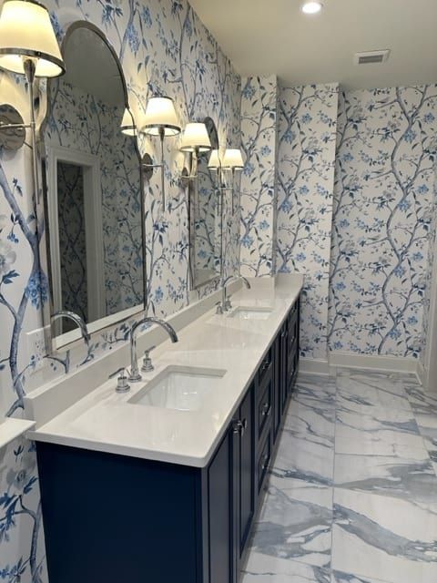 Bathroom with blue floral wallpaper, white countertops, dark blue cabinets, marble floor.