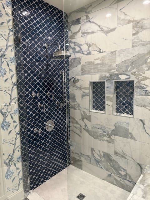 Elegant bathroom with blue patterned tile shower, marble walls, and built-in shelving.