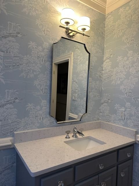 Bathroom with blue toile wallpaper, gray vanity, and decorative mirror.