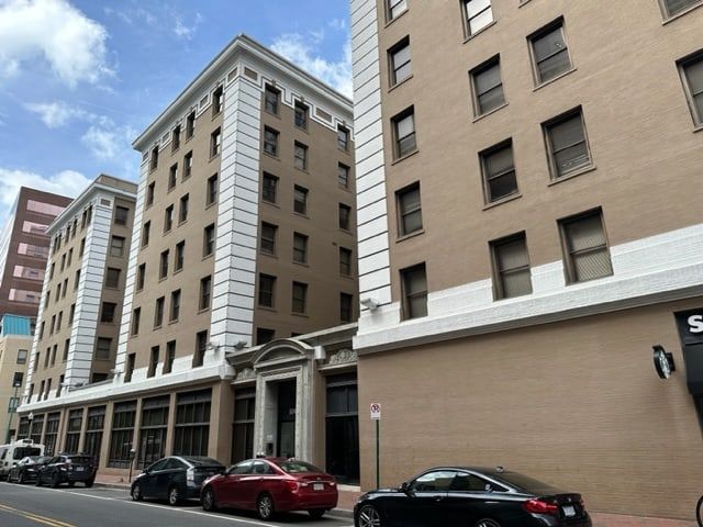 Brown apartment buildings with white trim, cars parked on the street, and a partly cloudy sky.