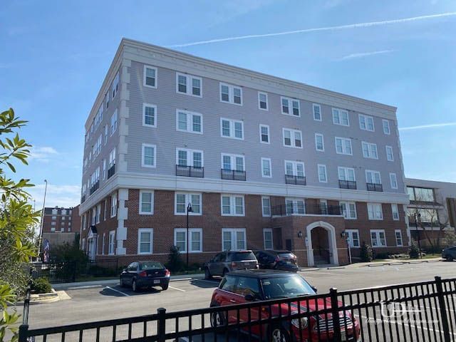 Apartment building with brick base, gray facade, and parked cars in front. Sunny day.