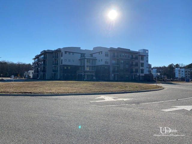 Multi-story apartment building under a bright sun, visible from a roundabout on a clear day.