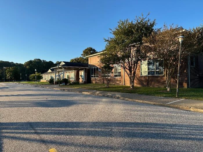 Brick building with trees in front, parked asphalt area, clear blue sky.