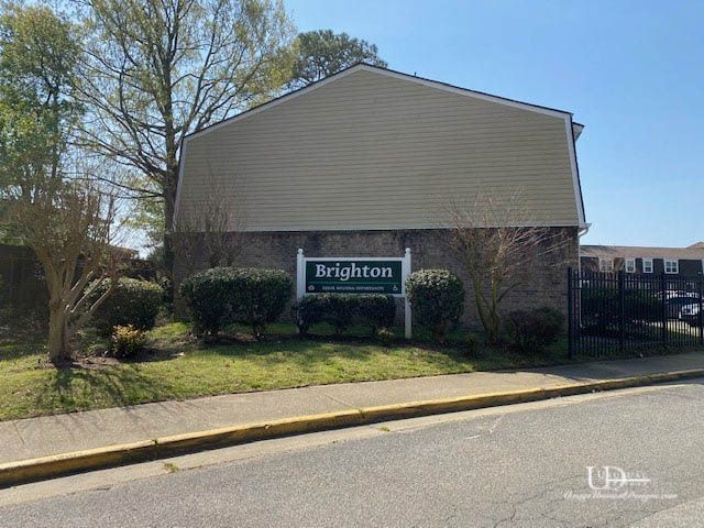 Brighton apartment complex sign with beige siding, shrubbery, and a fence.