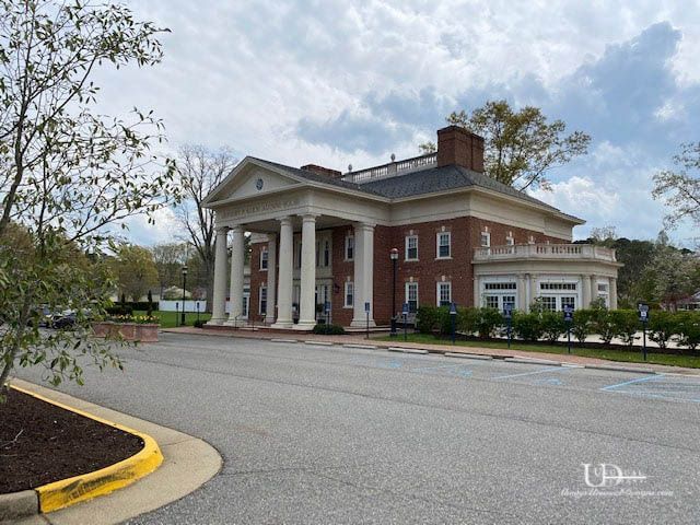 Brick and white columned building under a cloudy sky.