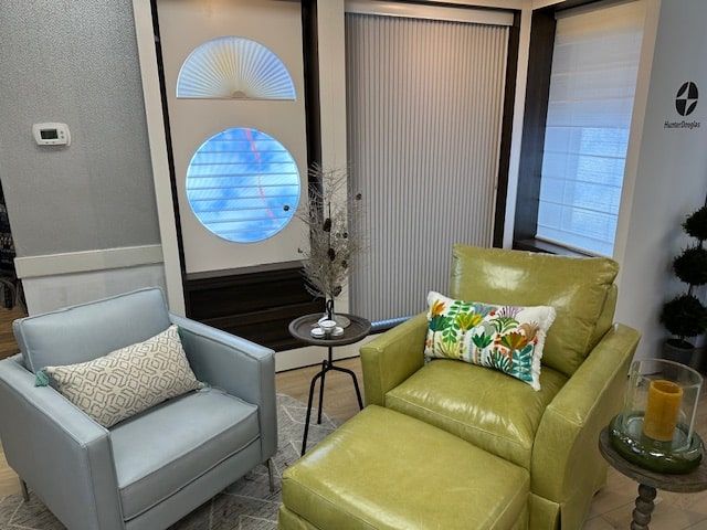 Two armchairs in a showroom with a decorative door and blinds. Green and blue seating, small table with decor.