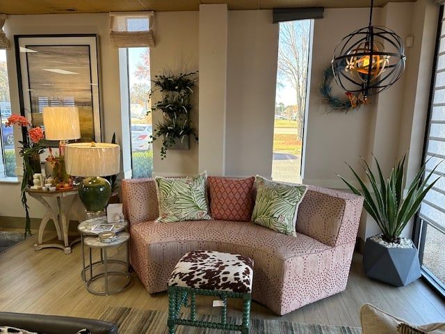 Living room setup: pink curved sofa, decorative pillows, small round tables, and a potted plant by a window.