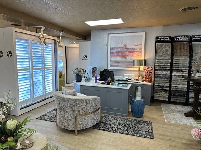 Interior of a window treatment showroom with displays, desk, and seating. Light colors, artwork, and various product samples are visible.