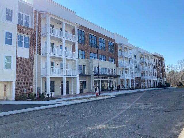 Multi-story apartment building with balconies, brick, and cream-colored siding. Clear sky, street in foreground.