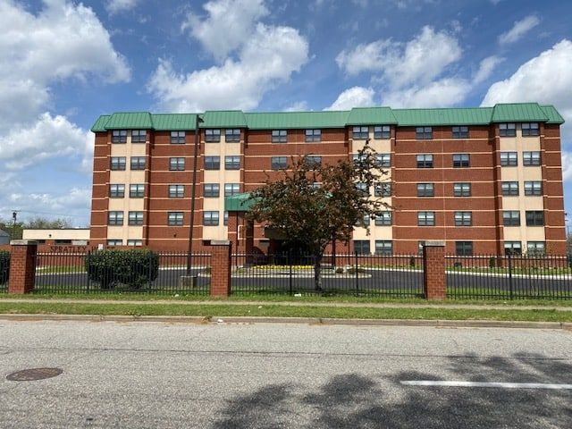 Brick apartment building with green roof, black fence, and cloudy sky.
