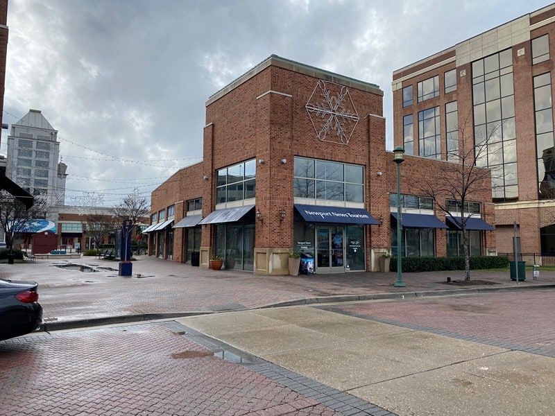 Brick commercial building with awnings, storefronts, and a glass front door, on a brick-paved street.