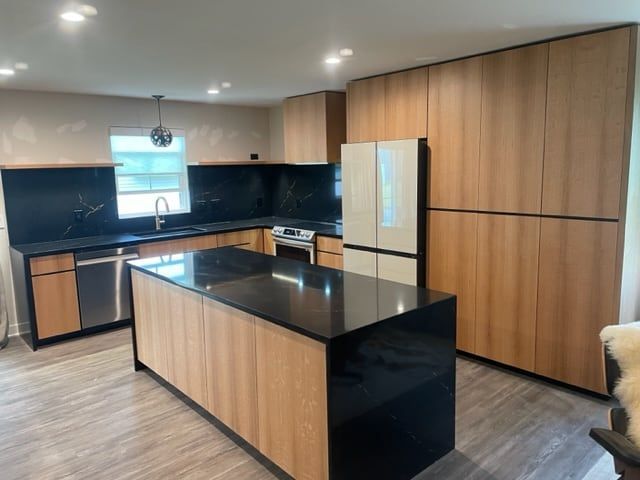 Modern kitchen with light wood cabinets, black countertops and island, and stainless steel appliances.