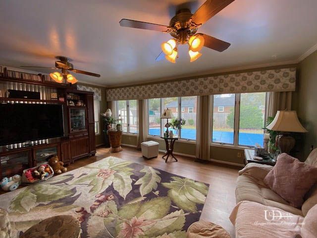 Living room with large floral rug, wooden entertainment center, windows, and ceiling fans.