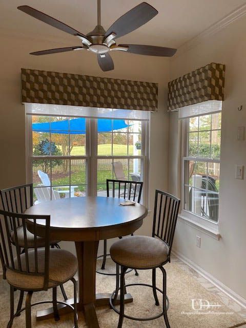 Breakfast nook with round table, four chairs, and geometric pattern valances. Large windows overlook backyard.