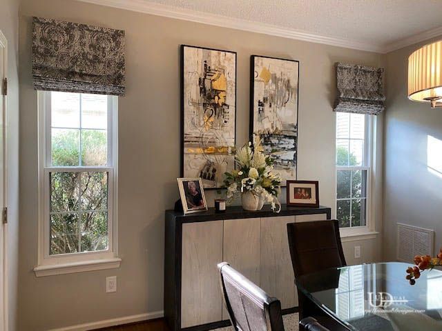Dining room with windows, art, and buffet. Grey and white floral Roman shades.