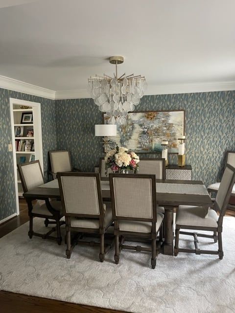 Dining room with a table, chairs, chandelier, artwork, and area rug. Teal patterned wallpaper.