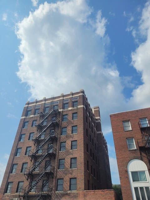 Tall brick building with external fire escape against a blue sky with fluffy clouds.