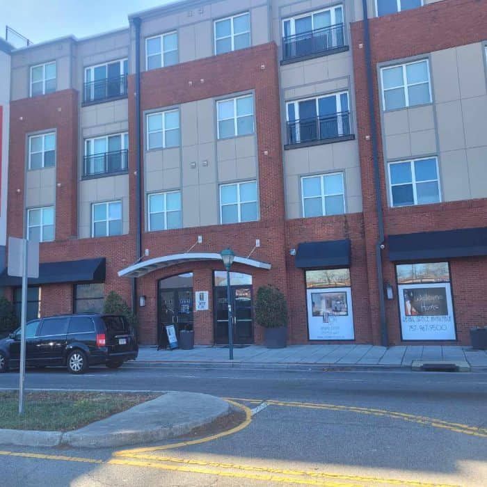 Apartment building with brick and tan facade, entrance canopy, black van parked.