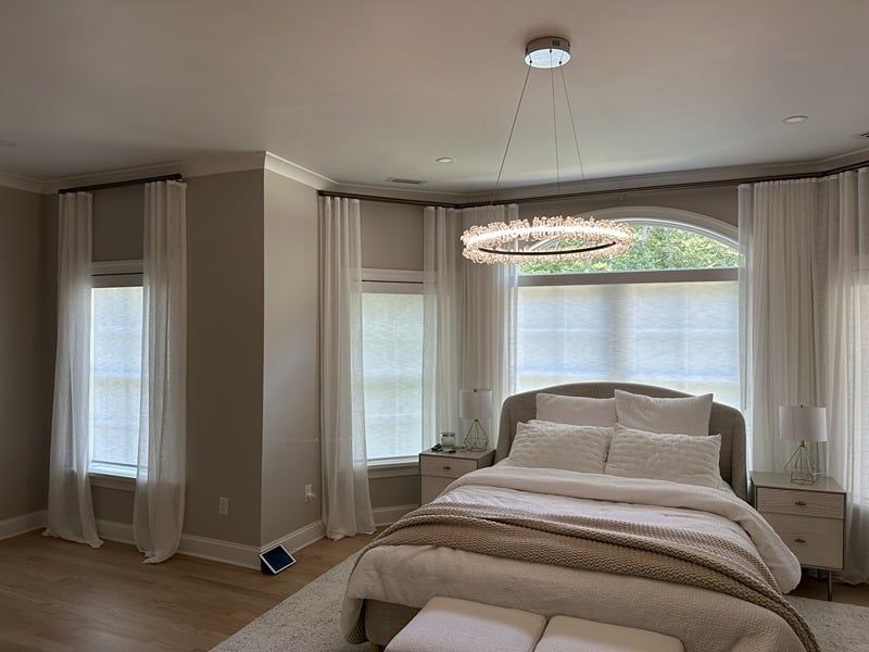 Bedroom with bed, sheer white curtains, and a sparkling chandelier.