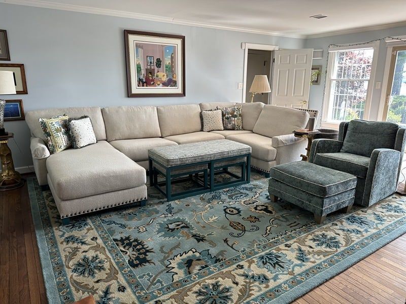 Living room with a large light-colored sectional sofa, teal rug, accent chair, and ottoman.