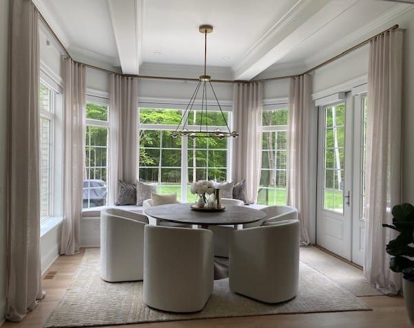 Elegant dining room with round table, white chairs, and large windows with cream curtains.