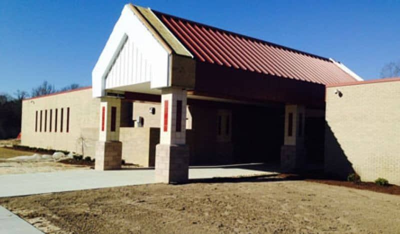 Brick building with red roof, awning, and concrete walkway. Bright, clear day.