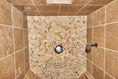 Shower stall with beige tile walls, pebble floor, and chrome fixtures.