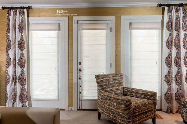 Three glass doors with white shades, patterned drapes, and a patterned armchair.