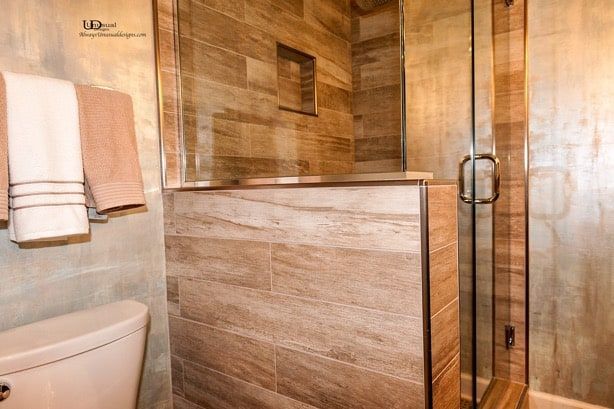 Bathroom with light brown tiled shower, glass door, toilet, and towel rack with beige towels.
