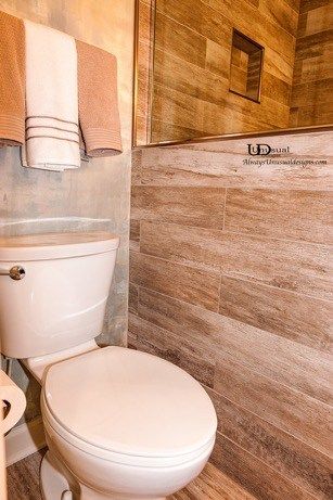 Bathroom with a white toilet, brown wood-look tile, and towels hanging on the wall.