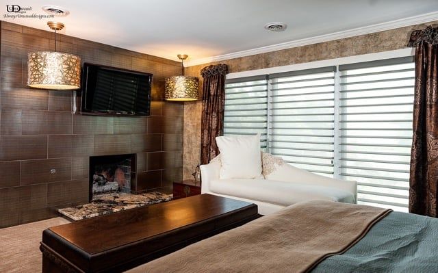 Cozy room with fireplace, TV, white chaise lounge, and gold drum pendant lights. Brown, gold, and white color scheme.