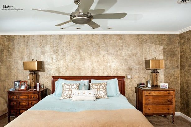 Bedroom with bed, nightstands, lamps, and ceiling fan against textured wall.