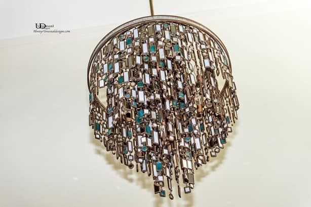 Ornate chandelier with rectangular, reflective accents and teal details, hanging from ceiling.