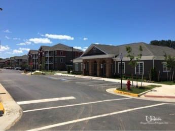 Apartment complex with asphalt road, parking spaces, and a clubhouse on a sunny day.