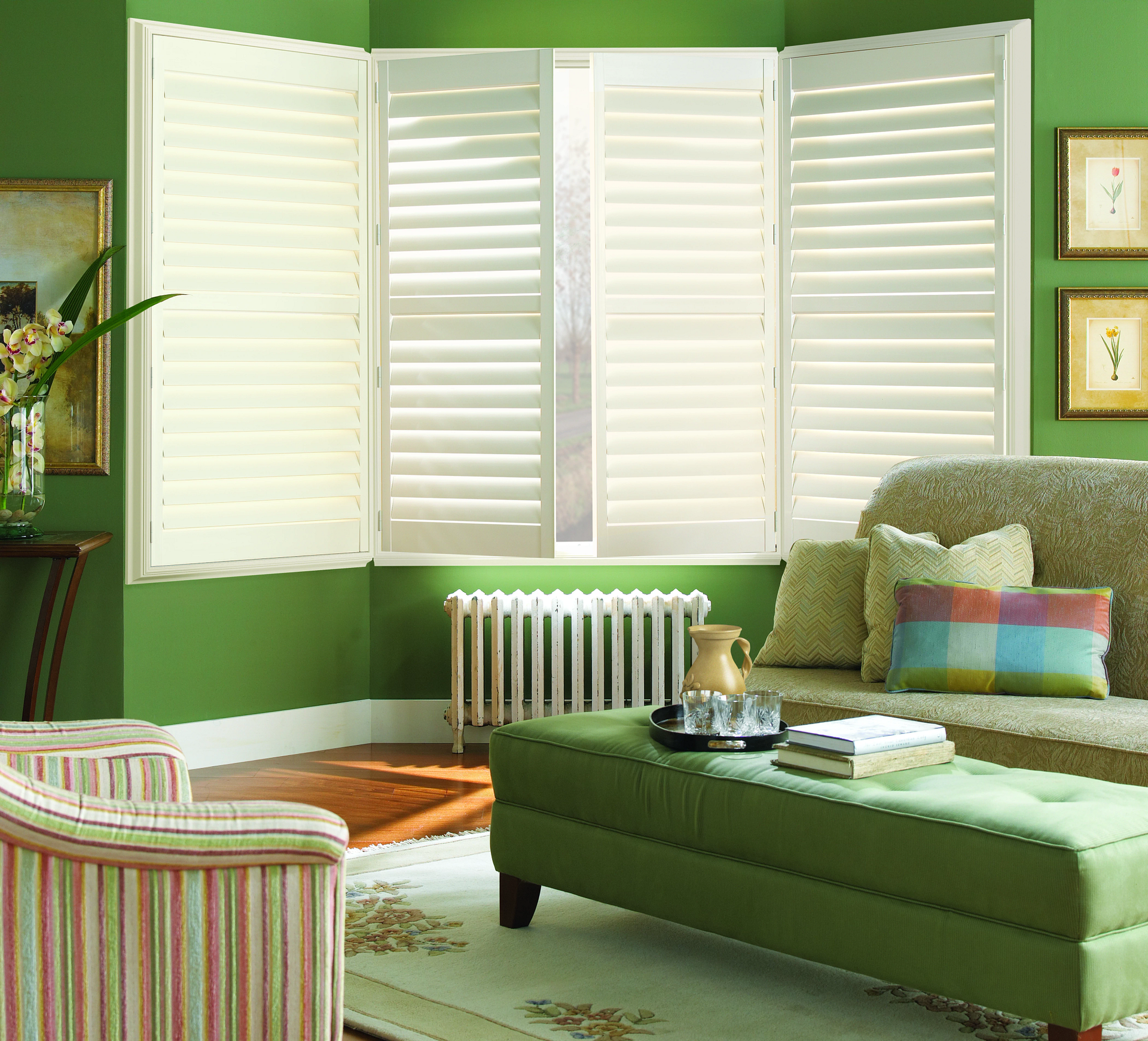 Living room with open white shutters, green walls, furniture, and a window.