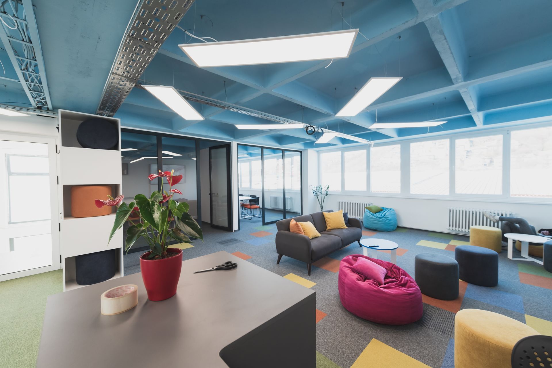 Modern office lounge area with colorful seating, large windows, and bright lighting.