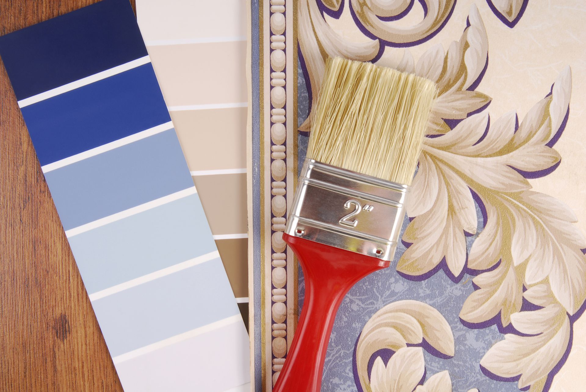 Paint swatches (blue, beige) and wallpaper with a paintbrush on a wooden surface.