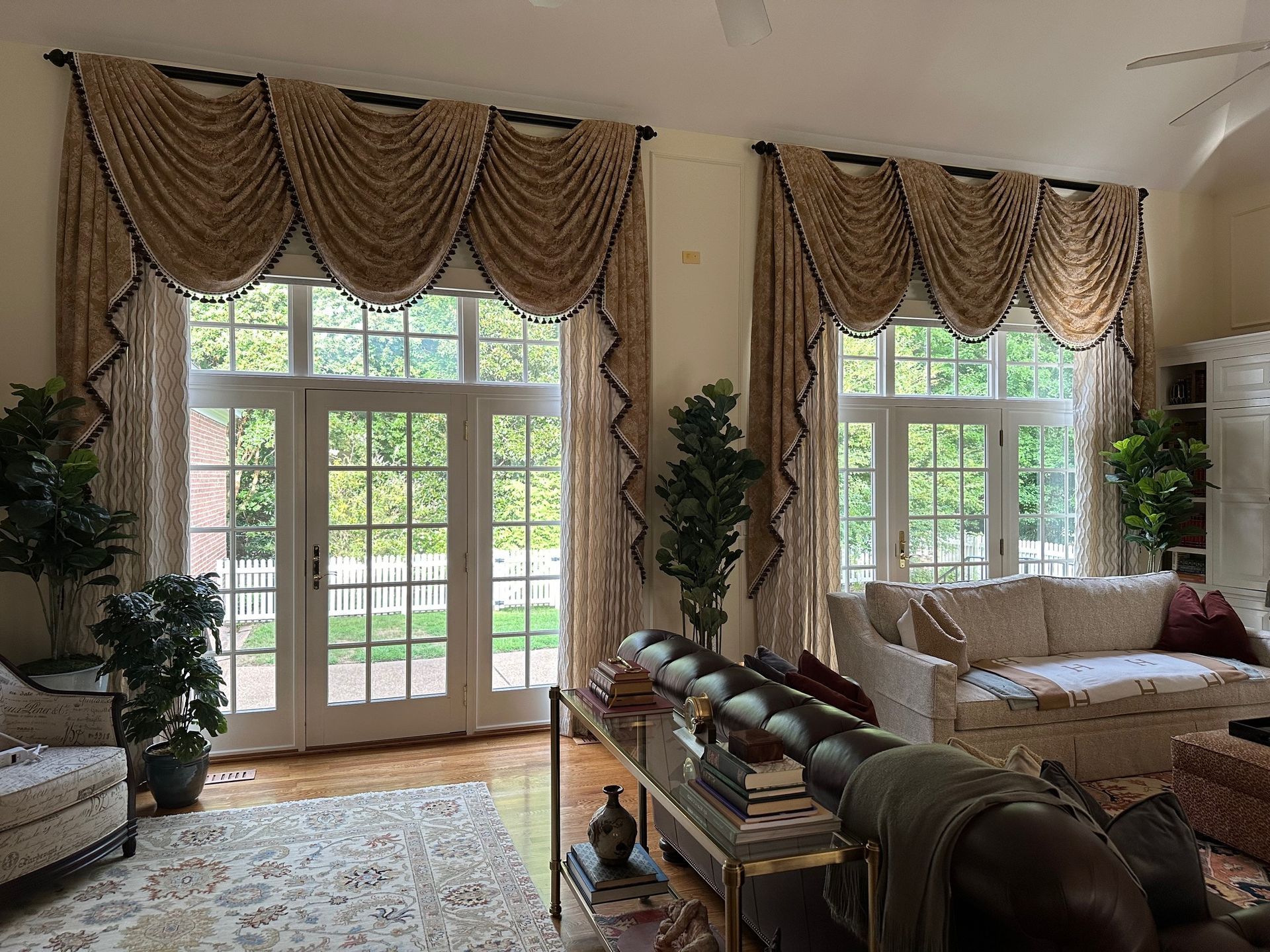 Living room with arched windows, draped curtains, and a view of trees through the glass doors.